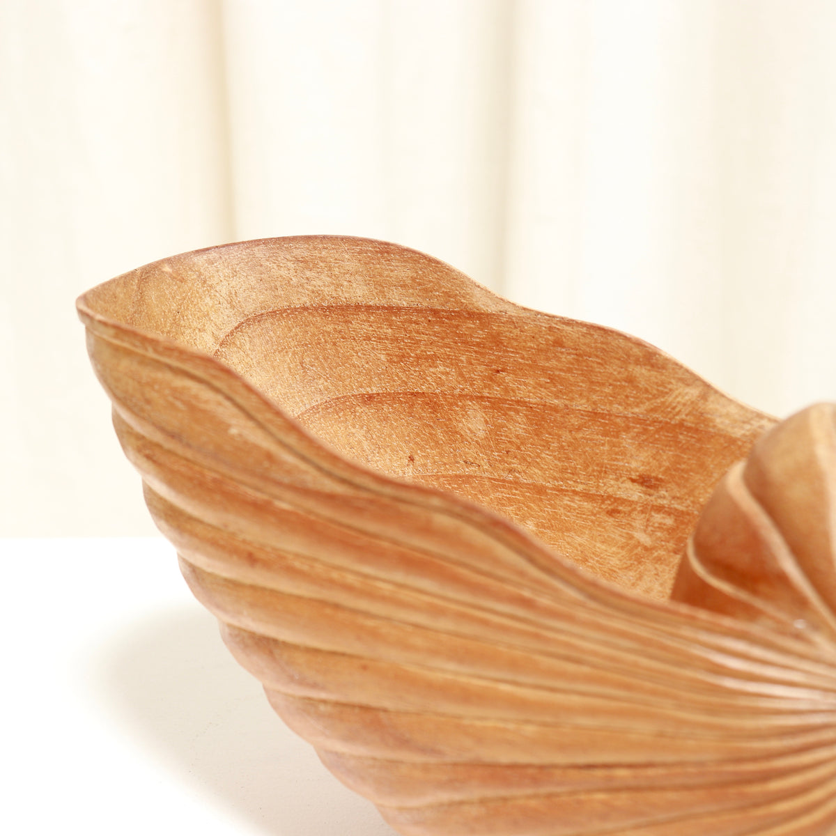 A close-up of a handcrafted wooden bowl with a leaf-like wavy rim and ribbed texture, shown on a light neutral background.