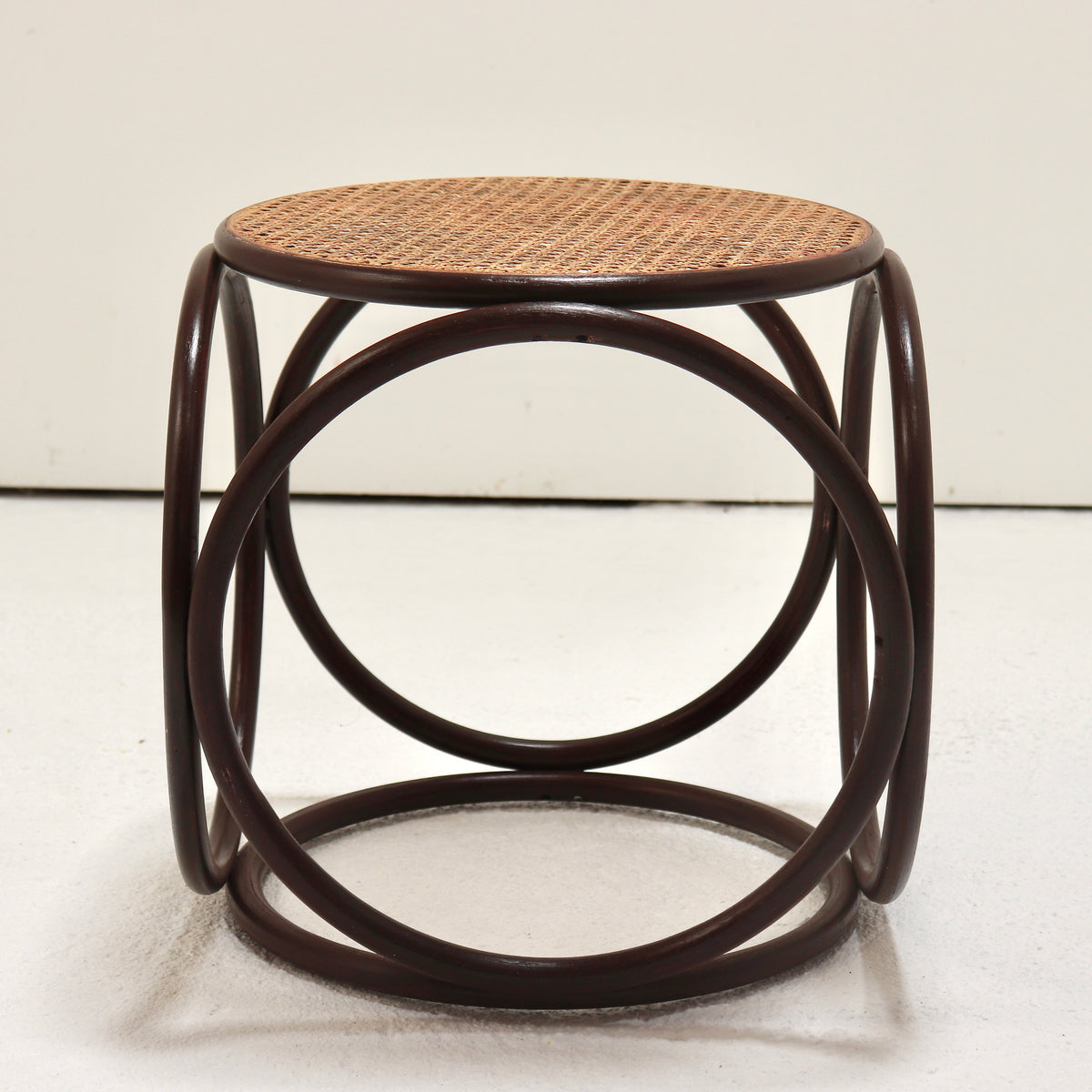 A round wooden stool with a dark brown bentwood frame and a natural woven cane seat, photographed against a plain off-white background.