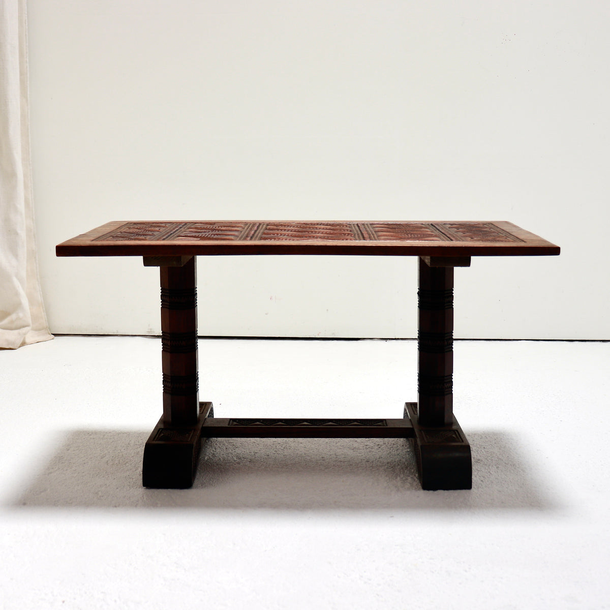 A dark brown wooden table with a carved geometric pattern top and turned legs, set against a plain white studio background.