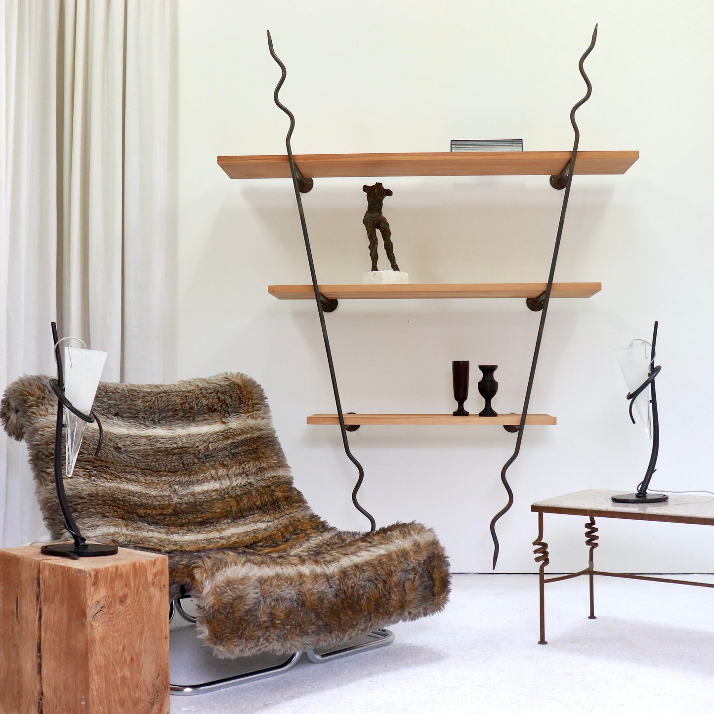 Shelving unit in a room setting with chair, lamp and table.