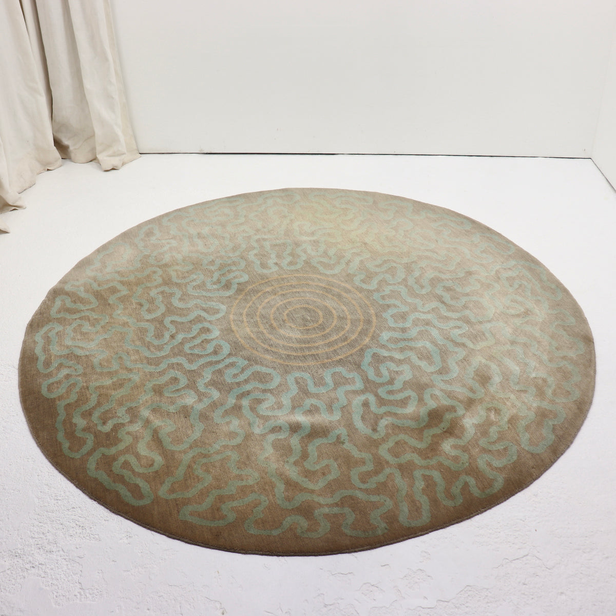 Full view of the circular wool rug showing its aqua ripple pattern, central peach rings and uneven fading.