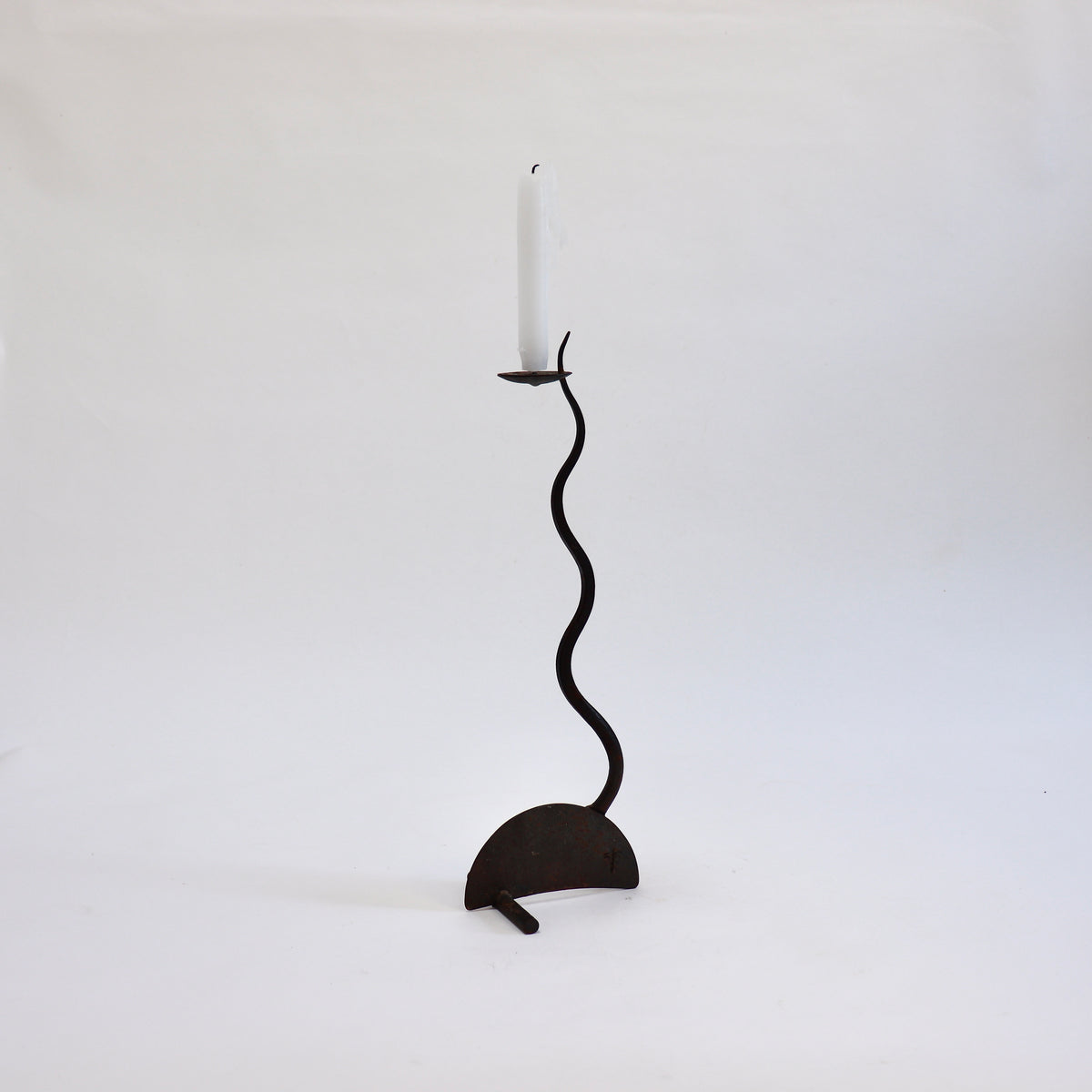 Reverse view of the sculptural iron candlestick showing its sinuous stem and transverse supporting foot.
