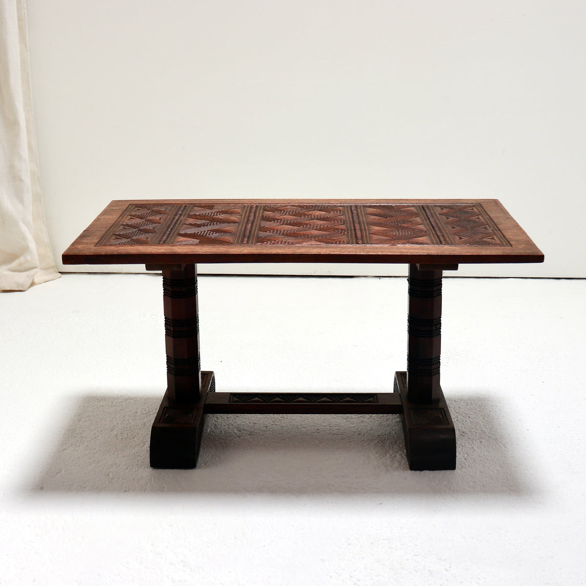 Front view of a Nigerian carved hardwood coffee table showing its two faceted supports and connecting stretcher.