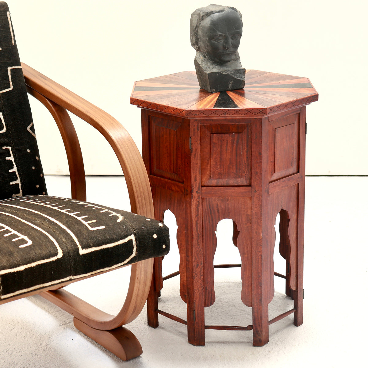 Anglo-Indian folding side table with a specimen-wood top, styled beside a wooden armchair with a stone sculpture.