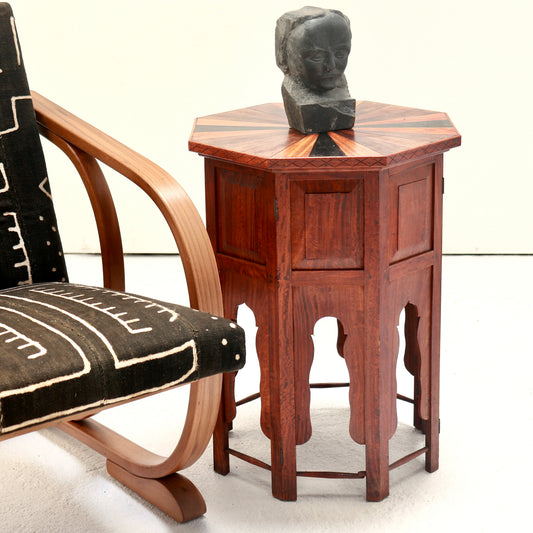Anglo-Indian folding side table with a specimen-wood top, styled beside a wooden armchair with a stone sculpture.