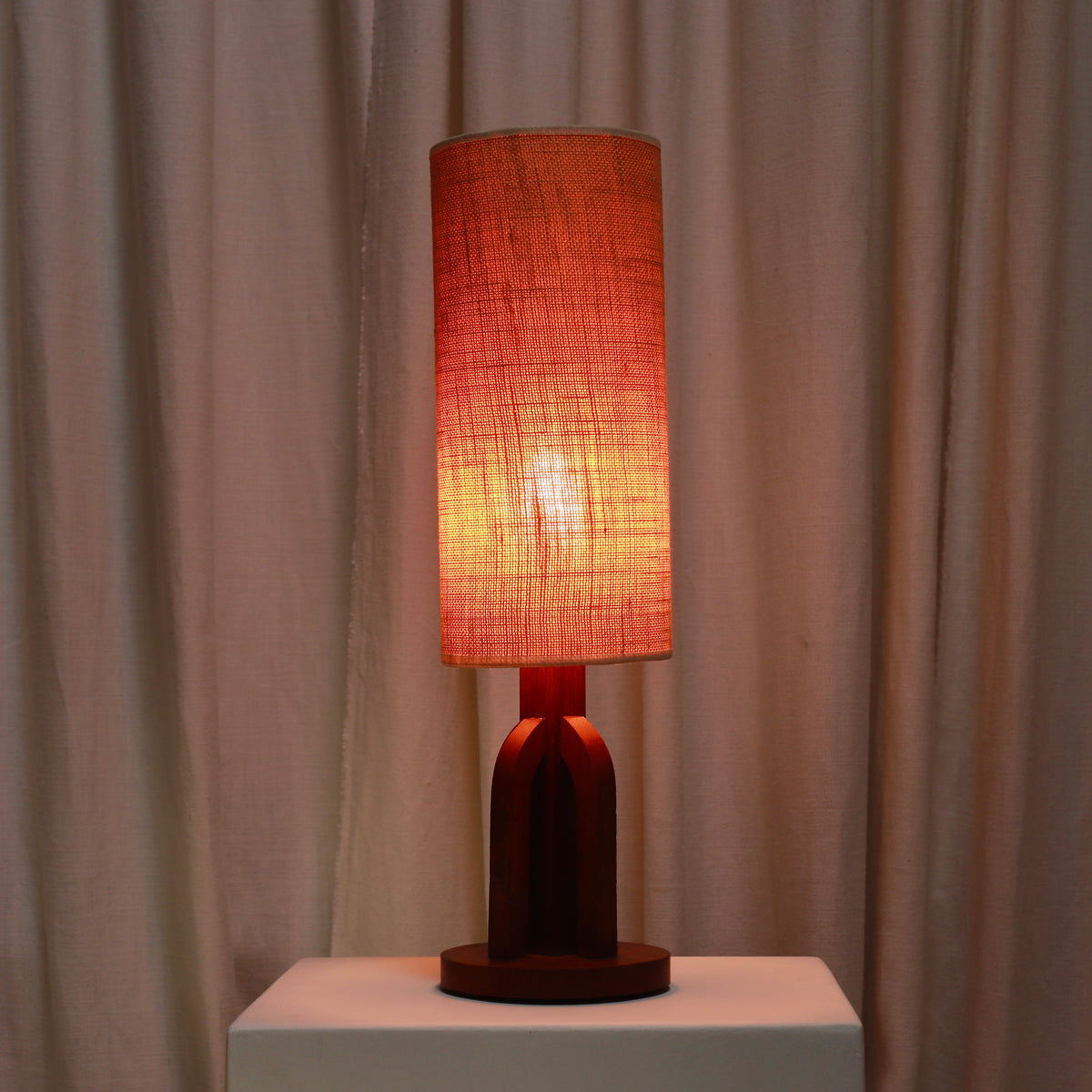 Oak table lamp illuminated with its tall fabric shade