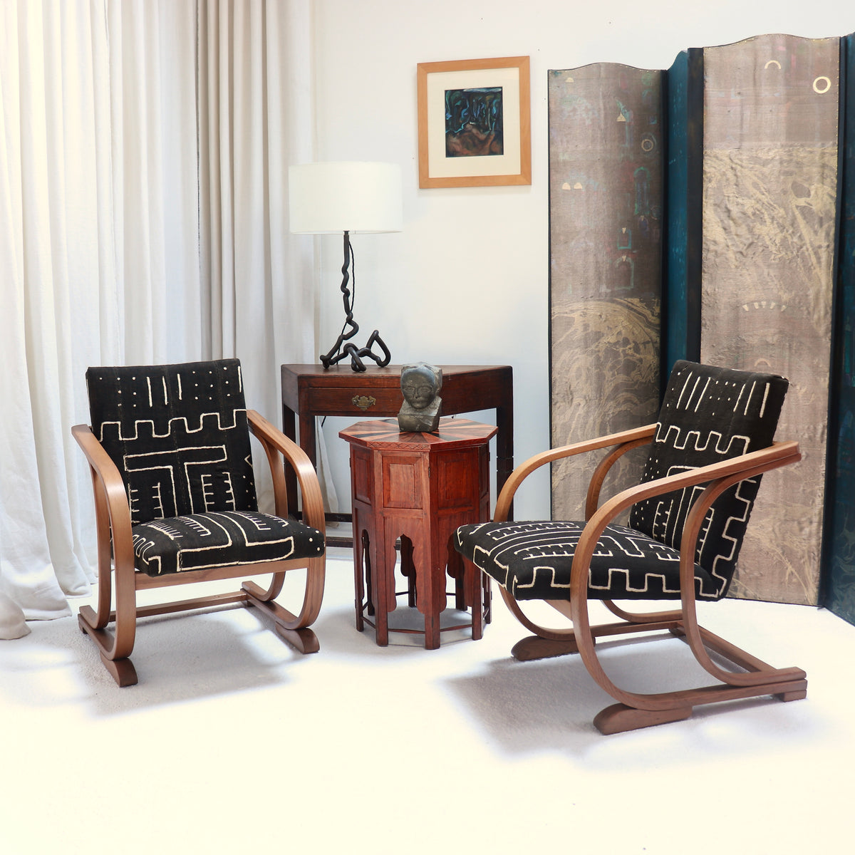 Pair of 1930s Heal’s bentwood armchairs upholstered in antique Malian mud cloth, arranged beside a wooden table in a furnished interior.