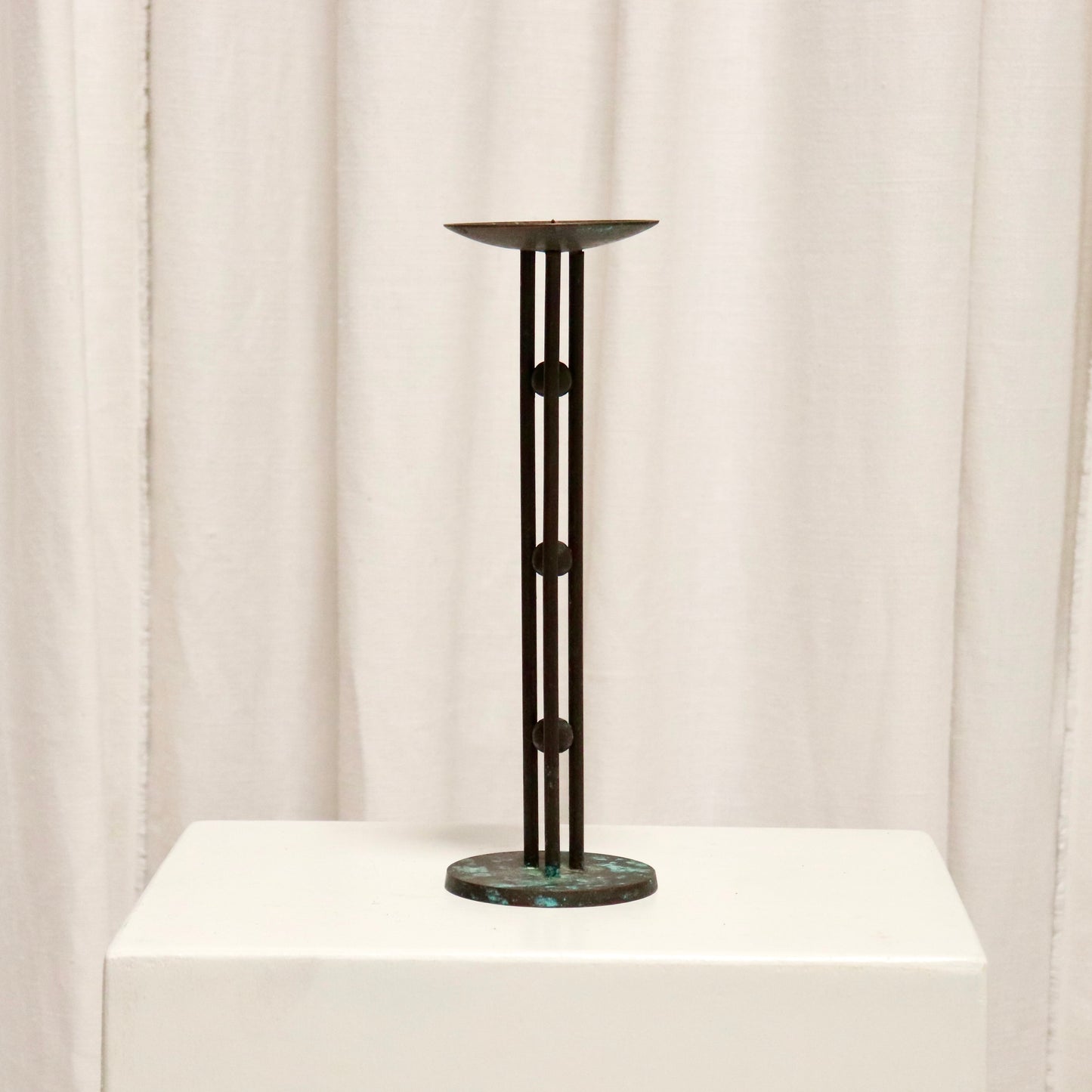 Full view of slim bronzed candlestick on plinth.