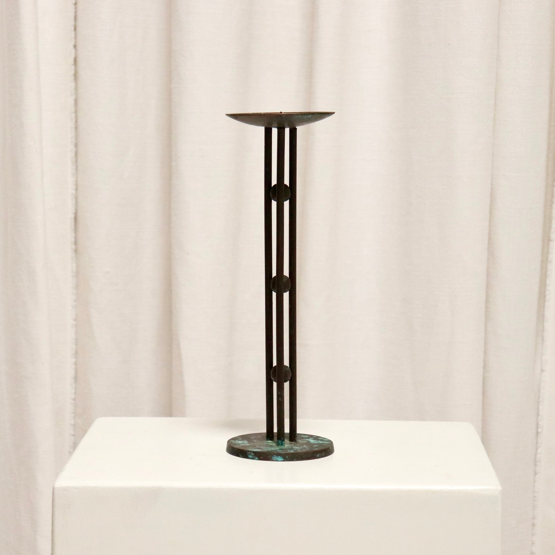 Full view of slim bronzed candlestick on plinth.