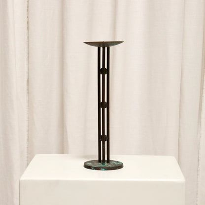 Full view of slim bronzed candlestick on plinth.