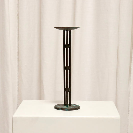 Full view of slim bronzed candlestick on plinth.