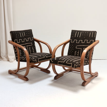 Pair of Heal’s bentwood armchairs viewed at an angle, showing sweeping curved arms and antique Malian mud cloth seats and backs.