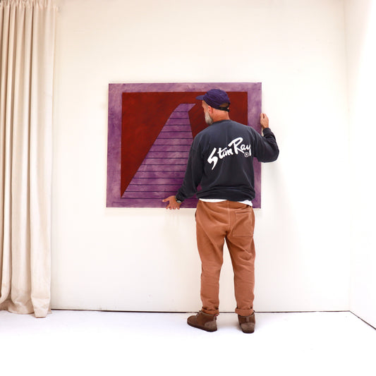 John Mitchell’s Square Pyramid, Capped, c.1984, held against a studio wall to show the scale of the violet and red oil painting.