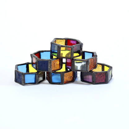 Six handmade stained glass napkin rings stacked to show their coloured glass panels