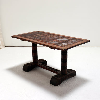 Three-quarter view of a Nigerian hardwood coffee table with a geometric chip-carved top and carved trestle base.