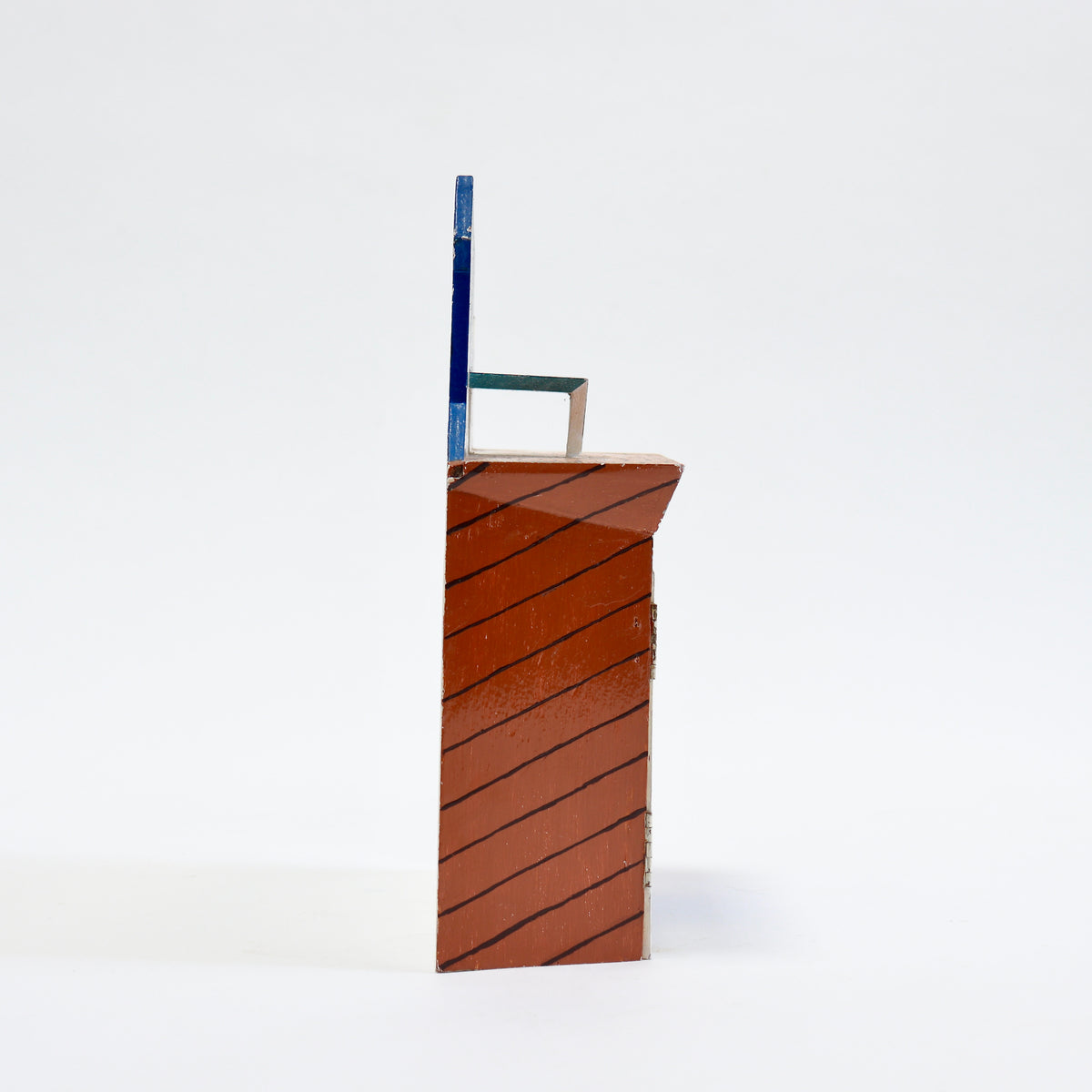 A small decorative architectural model or miniature building facade with a reddish-brown tiled base, black diagonal stripe pattern, and a blue vertical element on a white background.