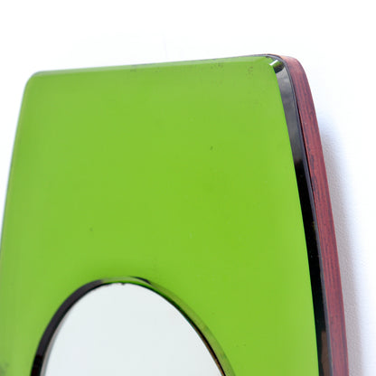 Close-up of an art deco wall mirror with a bright lime green glass panel and a dark reddish-brown wood frame, showing a small portion of the circular mirror reflection.