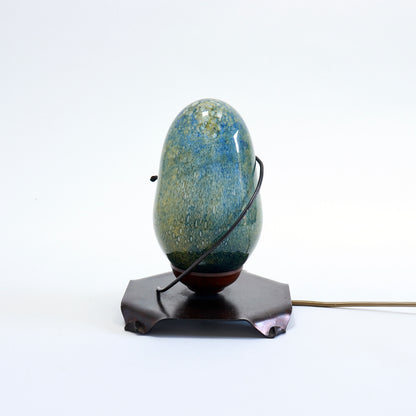 Side view of sculptural glass lamp showing its curved metal retaining arm