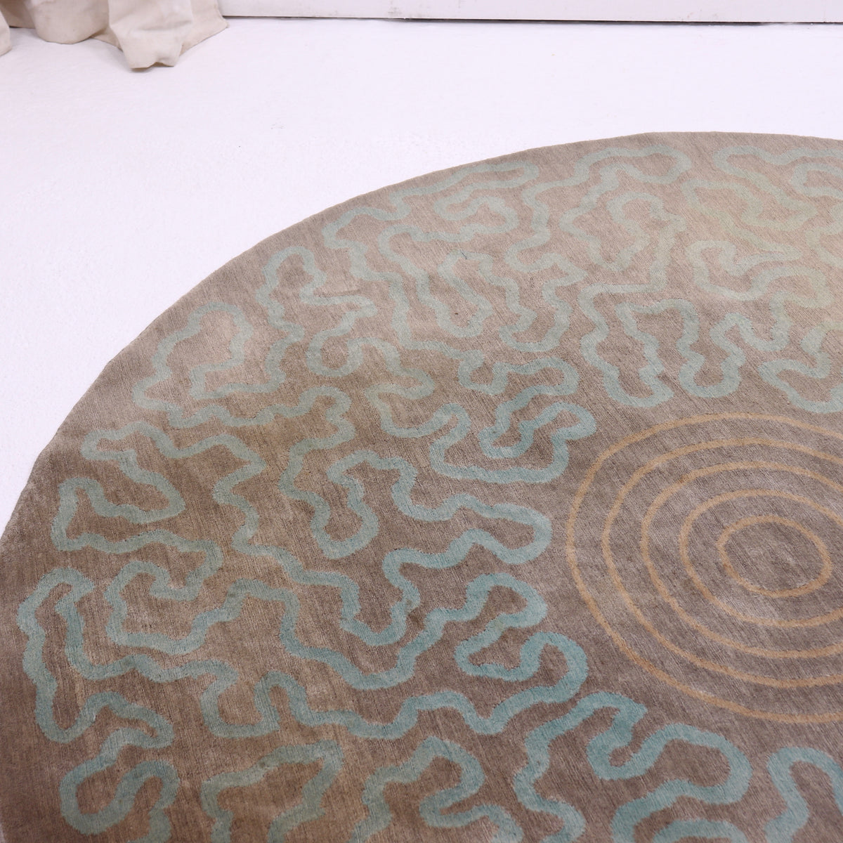 Detail of the rug’s aqua squiggles and central rings, with variations in the taupe ground colour.