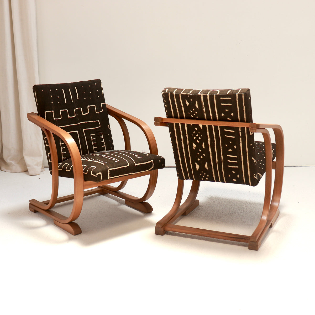 Front and rear views of restored Heal’s Art Deco armchairs, showing curved wooden frames and patterned Malian mud cloth upholstery.