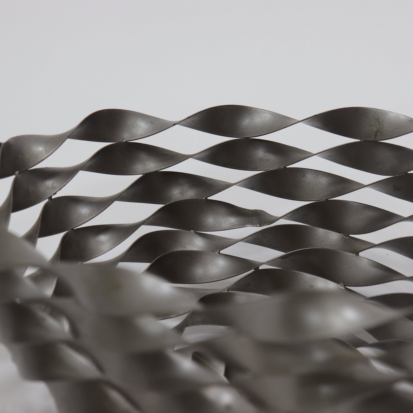 Close-up of woven steel ribbon structure with industrial finish
