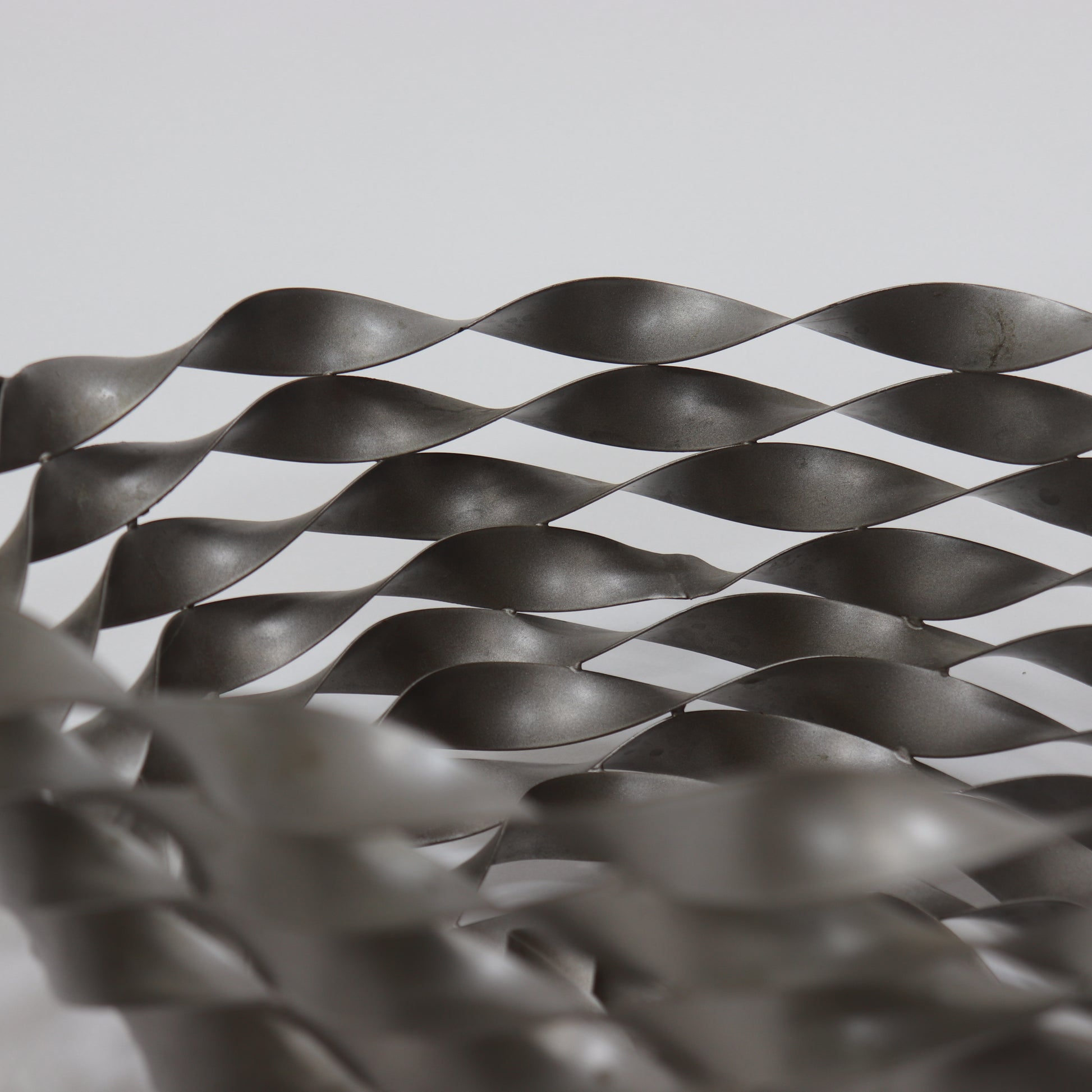 Close-up of woven steel ribbon structure with industrial finish
