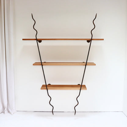Sculptural wrought-iron wall shelves with three timber boards against a white wall.