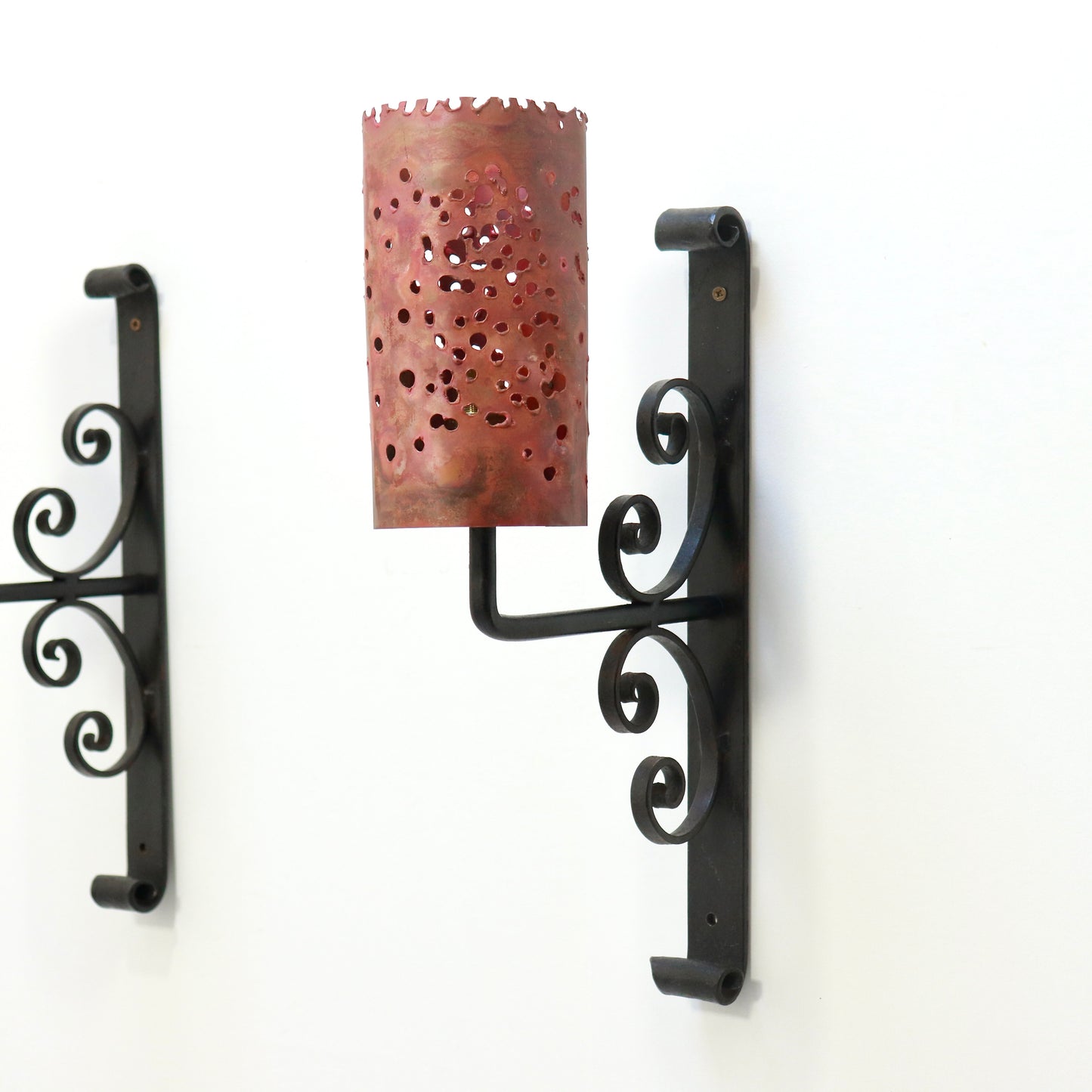 Single sconce angled view showing torch-cut copper shade and iron scroll backplate