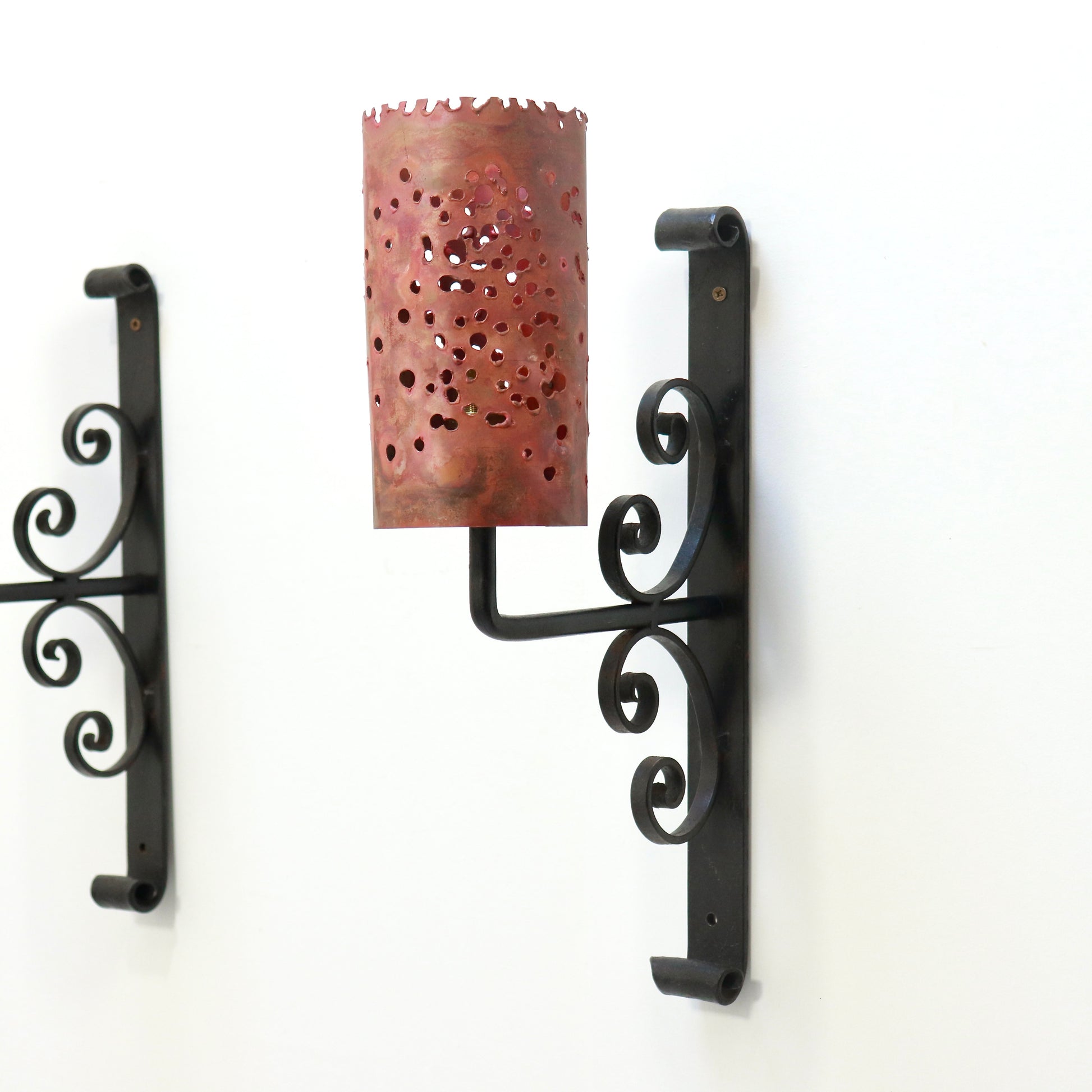 Single sconce angled view showing torch-cut copper shade and iron scroll backplate