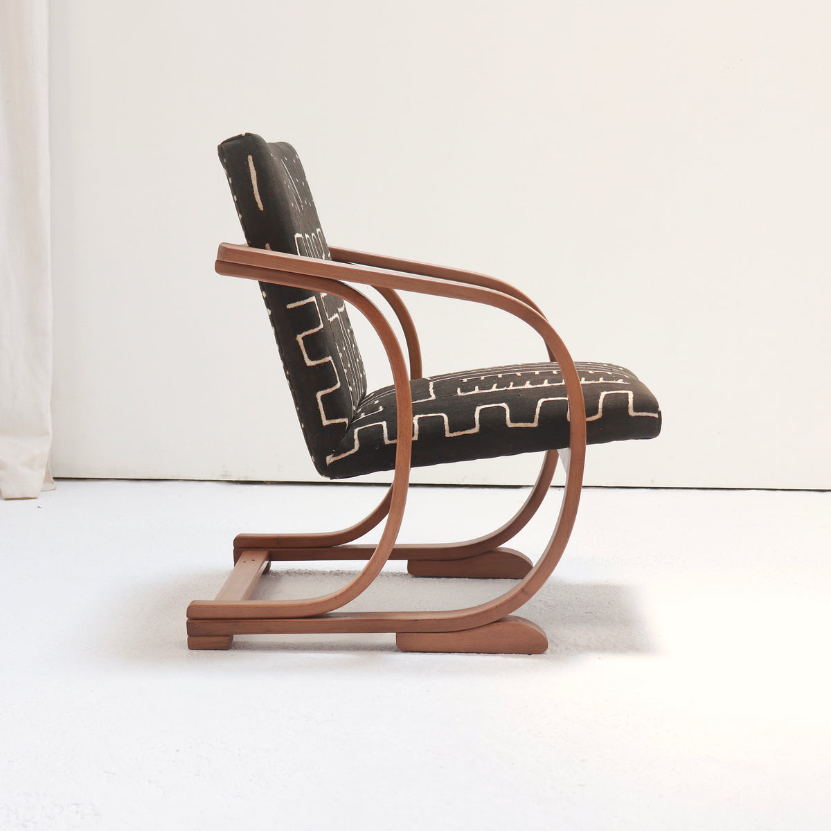 Angled view of a Heal’s Art Deco armchair with curved wooden arms and geometric antique mud cloth upholstery.
