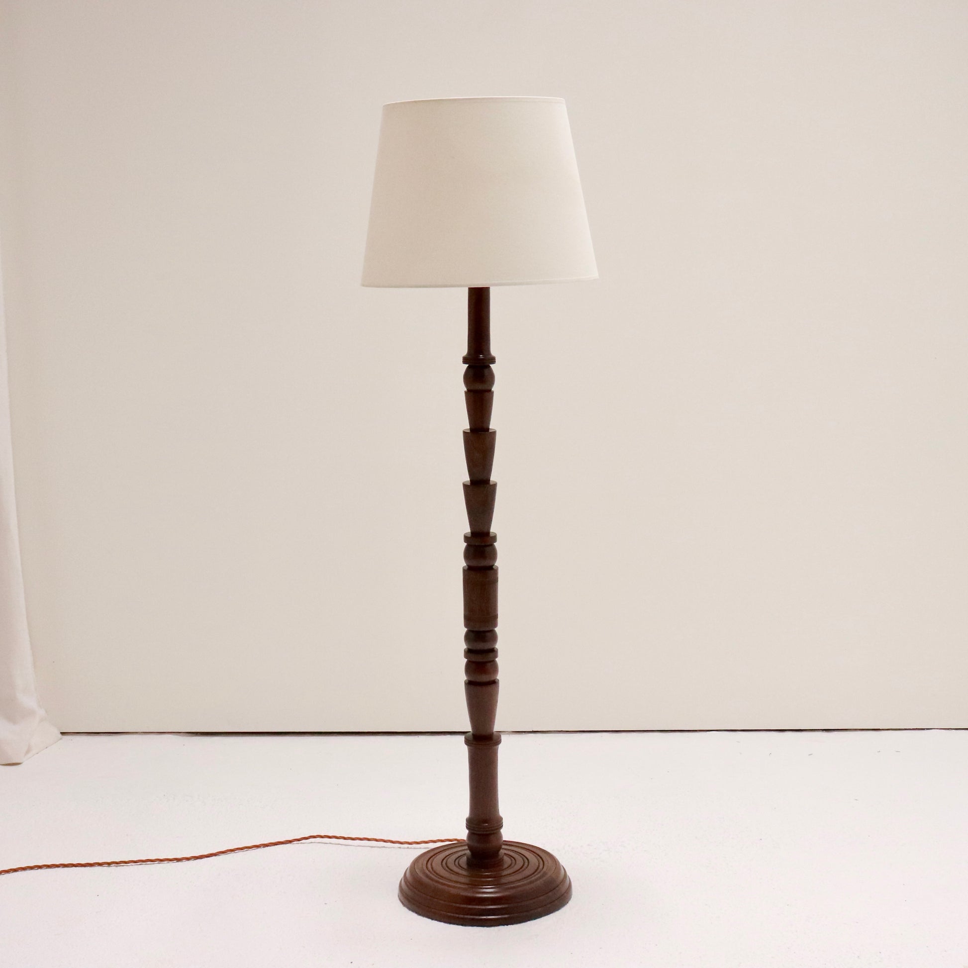 Vintage turned walnut floor lamp with linen shade on white backdrop.