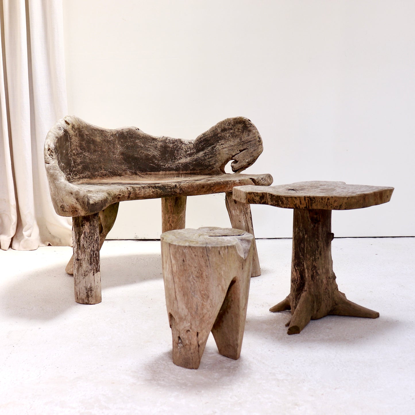 Primitive carved hardwood garden seating set comprising bench, side table and stool.