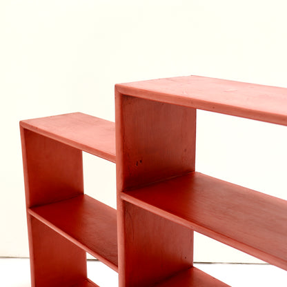 A close-up of a red wooden shelving unit with open cubby compartments, photographed against a plain off-white background.