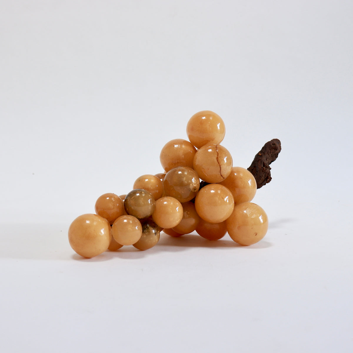 End view of the clustered alabaster grapes with the dark wooden stem projecting towards the right.