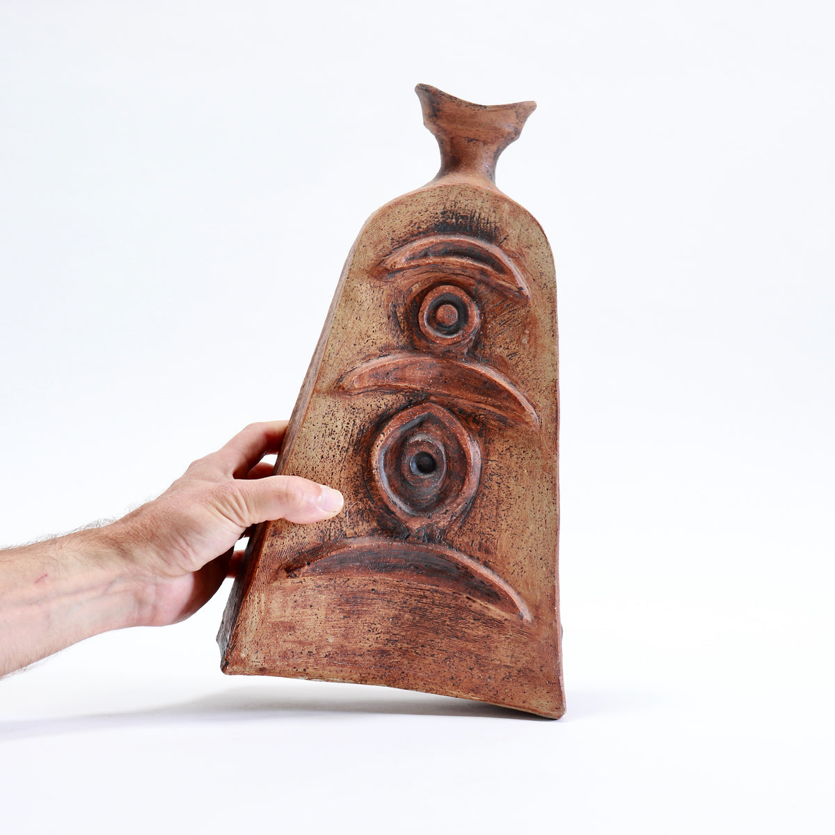 Hand holding a 35 cm tall Cornish pottery vessel to show its scale and sculptural relief decoration.