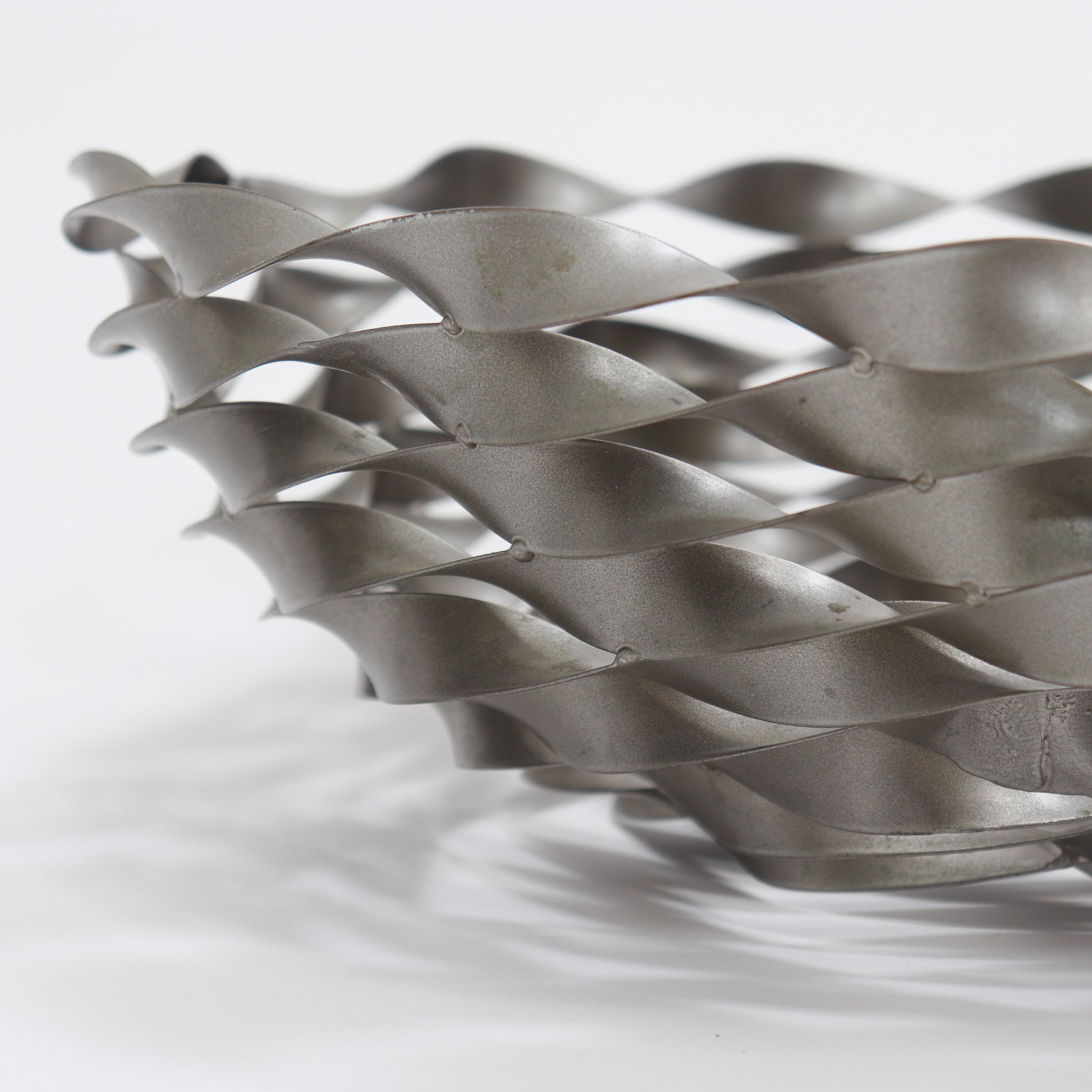 Twisted ribbon steel bowl casting patterned shadows on surface