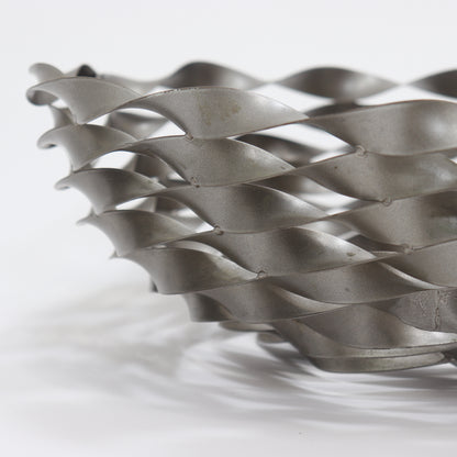 Twisted ribbon steel bowl casting patterned shadows on surface