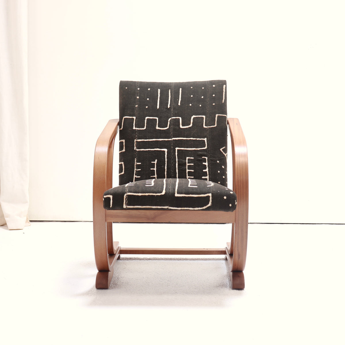 Front view of a restored Heal’s bentwood armchair upholstered in dark antique Malian mud cloth with cream stepped lines and dots.