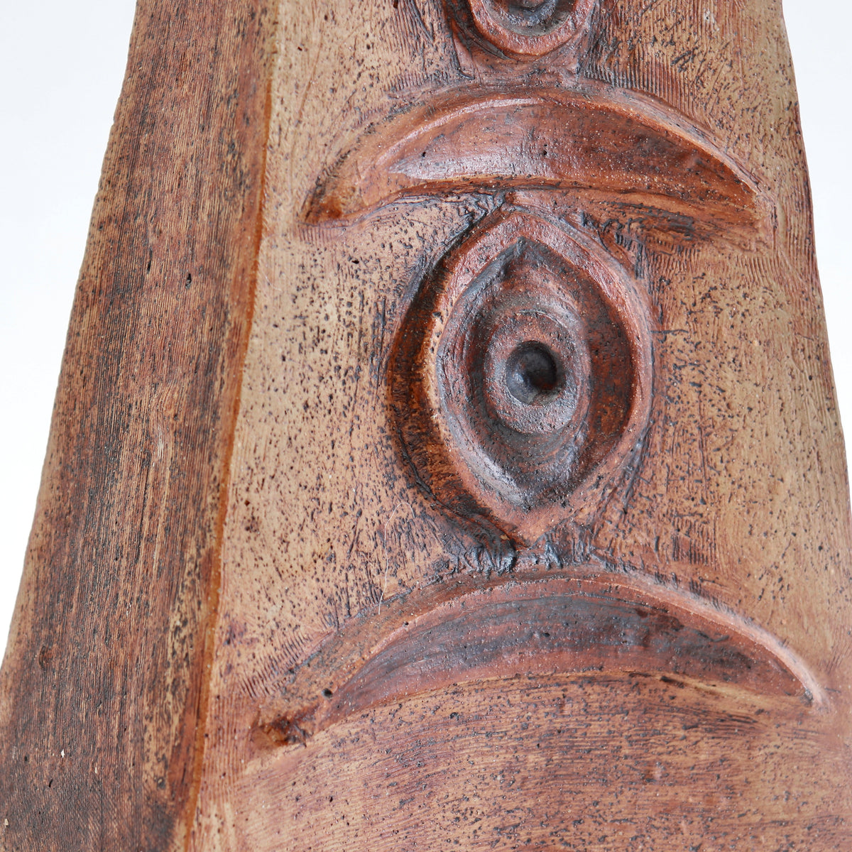 Detail of raised crescent and circular motifs on a Cornish pottery vessel, with dark accents across the textured clay surface.