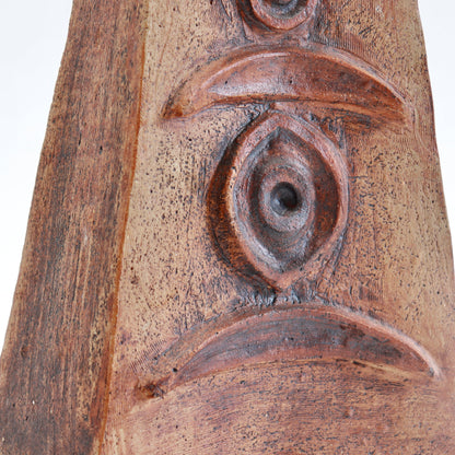 Detail of raised crescent and circular motifs on a Cornish pottery vessel, with dark accents across the textured clay surface.