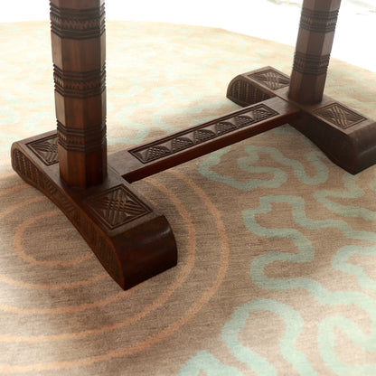 Dark brown carved wooden table legs and base on a patterned beige and light blue rug.