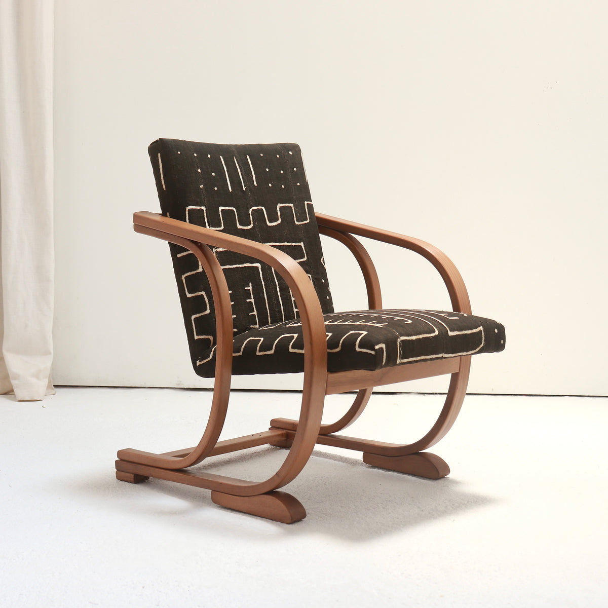 Side profile of a 1930s Heal’s armchair showing its looping bentwood frame, inclined upholstered back and compact proportions