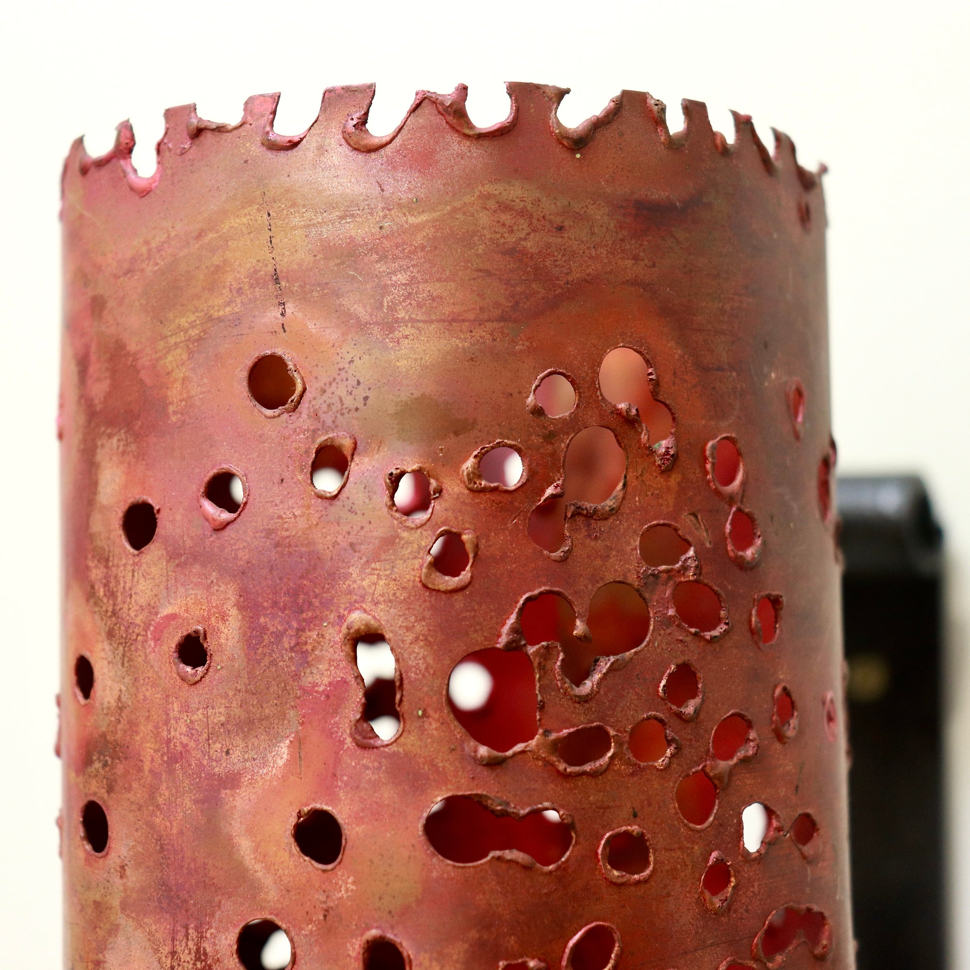 Detail of jagged top edge and mottled red-bronze patina on copper cylinder