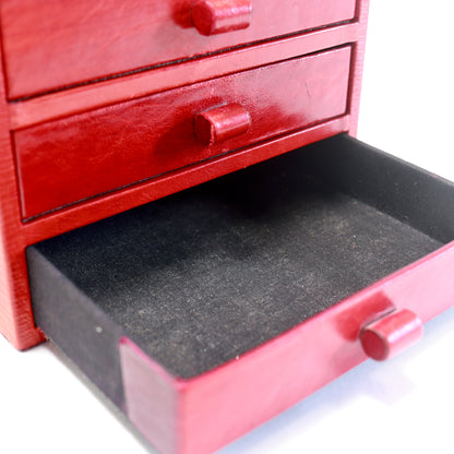 A close-up of a red wooden jewelry box with two drawers, one of which is open to reveal a black velvet-lined interior, on a white background.
