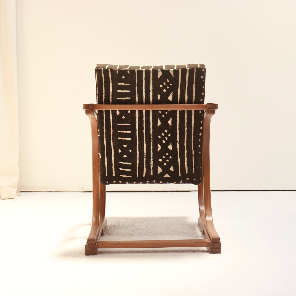 Rear view of a Heal’s bentwood armchair showing mud cloth upholstery with vertical stripes, small geometric motifs and a wooden cross rail.