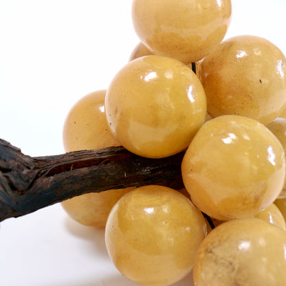 Detail of honey-coloured alabaster grapes gathered around a rough, dark wooden stem.
