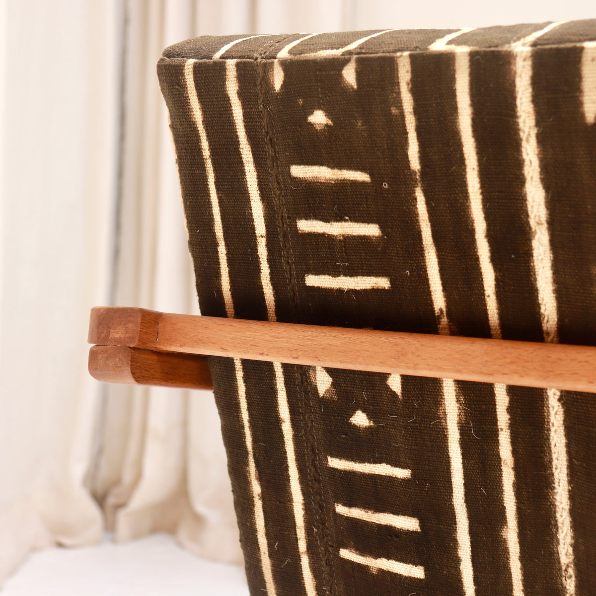 Detail of the wooden rear cross rail and upholstered back of a Heal’s armchair, showing pale motifs on dark Malian mud cloth.