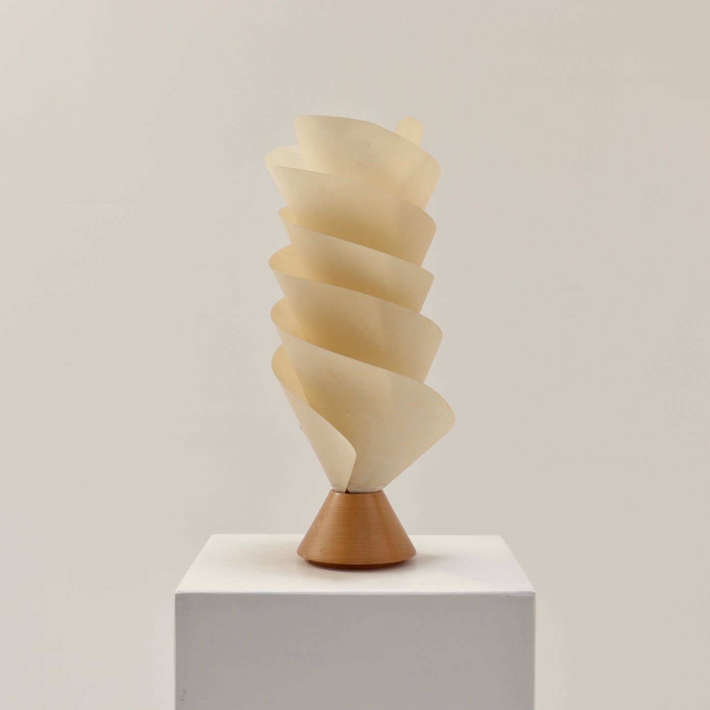 Postmodern spiral parchment table lamp with wooden base, 1980s design, sculptural lighting object on white plinth.
