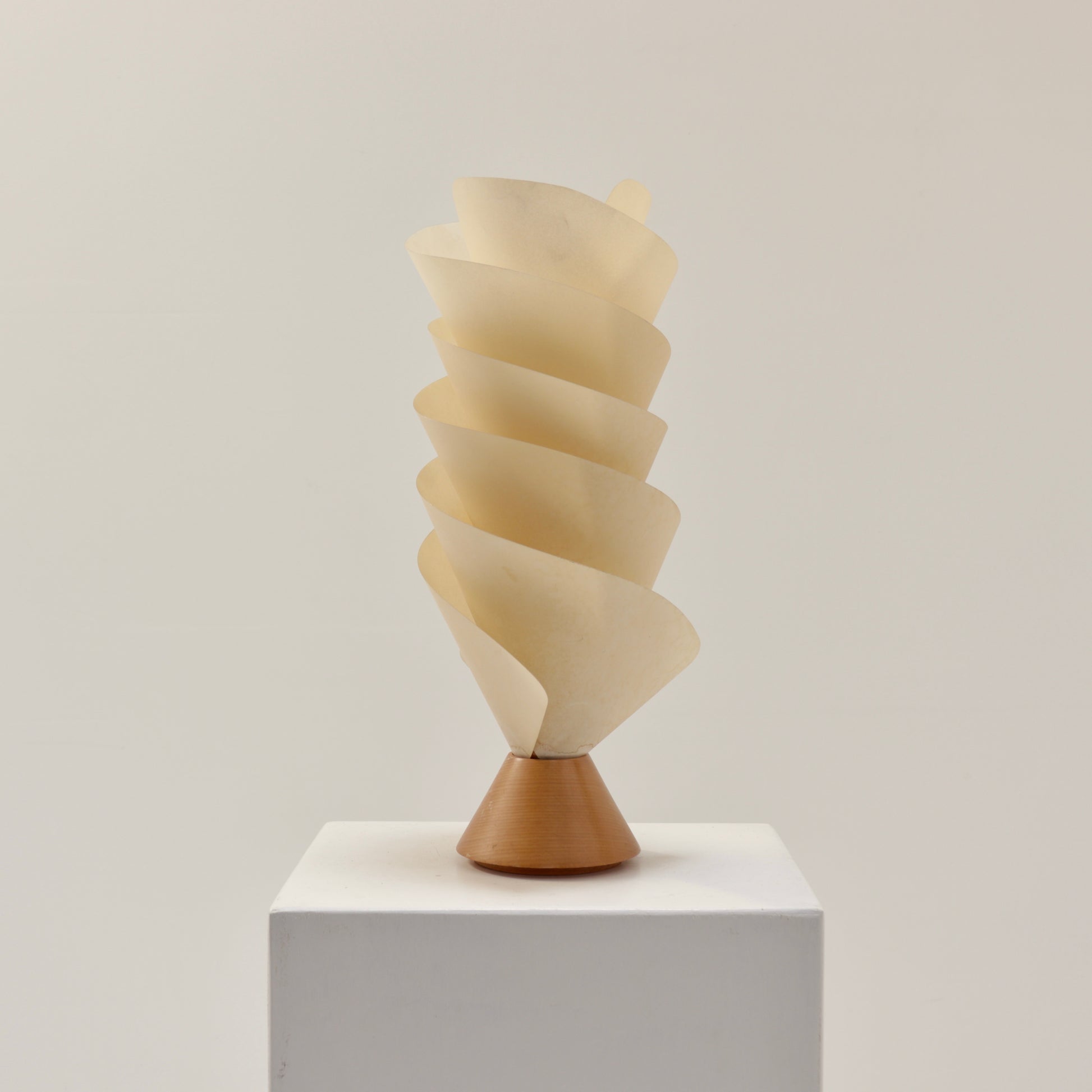 Postmodern spiral parchment table lamp with wooden base, 1980s design, sculptural lighting object on white plinth.