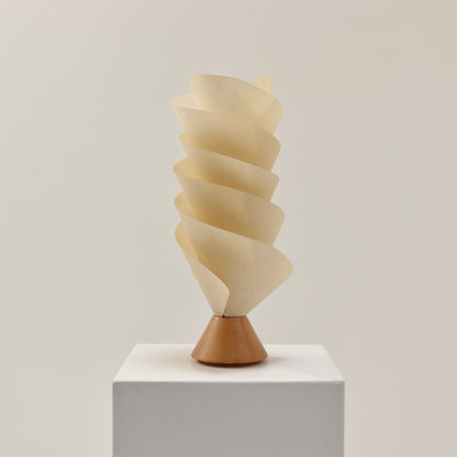 Postmodern spiral parchment table lamp with wooden base, 1980s design, sculptural lighting object on white plinth.